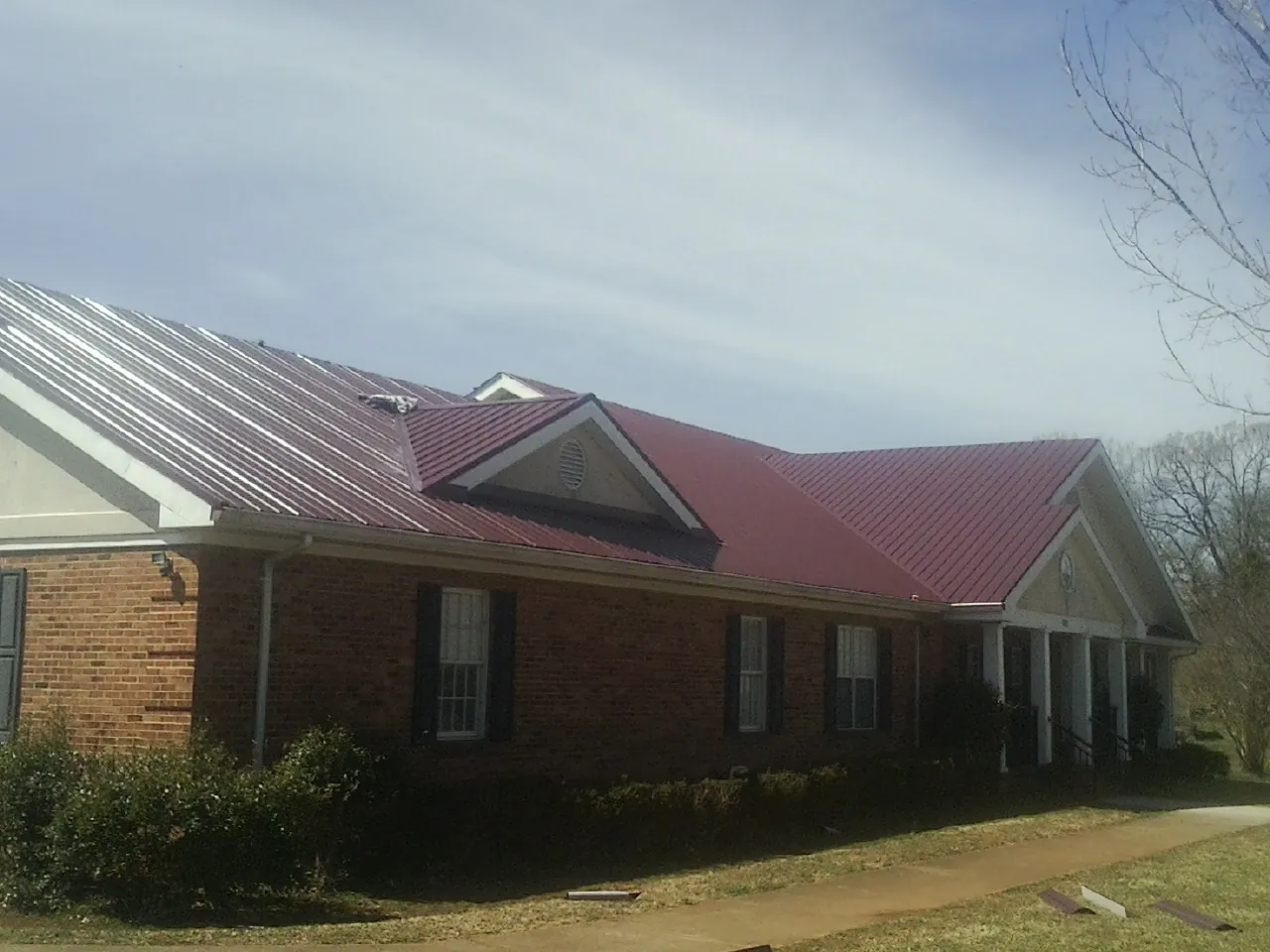 Red metal roof with gabled entries on a long brick building, from a Hail Damage Roof Repair job in Grove City