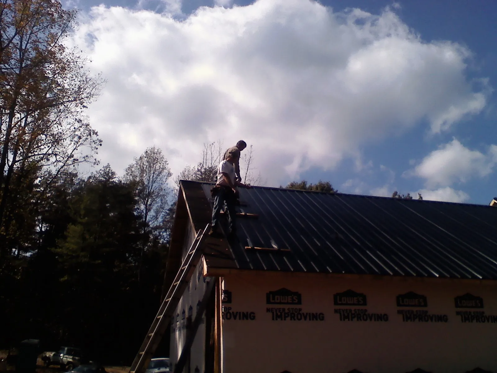 Roofer fastening dark metal panels high against a cloudy sky, from a Roof Inspection job in Grove City